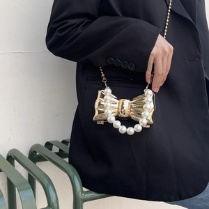 Dettaglio borsa a fiocco dorata con manico di perle e catena su un blazer nero elegante