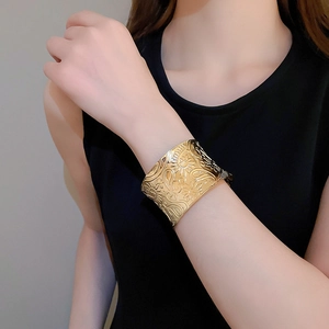 Macro view of wide gold cuff bracelet featuring vintage sun and floral embossed patterns