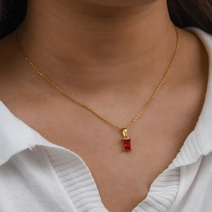 Détail d'un collier en chaîne dorée avec un pendentif en zircon rouge rectangulaire