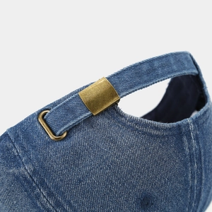Detailed macro view of the adjustable bronze metal buckle on a blue denim baseball cap