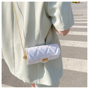 Close-up of white quilted cylinder bag with gold chain strap on a green suit