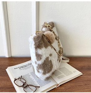Detail of plush cow print tote bag with gold chain strap and fluffy ball charm accessory