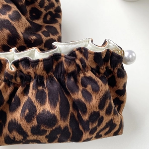 Detail of leopard print fabric pouch featuring a drawstring closure and a white pearl charm