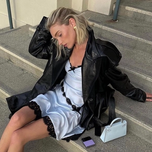 Dettaglio dell'abito in pizzo blu con trench in pelle nera e borsa a mano bianca di classe