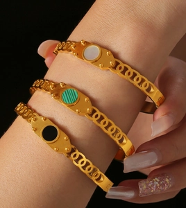 Close-up of gold titanium bracelets with white shell, green and black geometric inlays