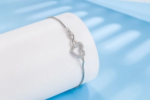Close-up of silver heart and infinity symbol bracelet with crystals on a stand