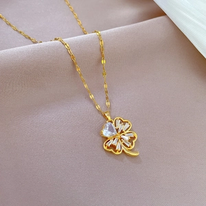 Golden clover pendant necklace with heart-shaped zircon on pink silk fabric background