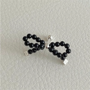 Detail of a black beaded bow stud earring crafted in S925 silver on white leather