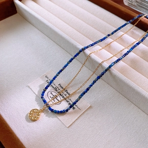 Close-up of double-layered necklace with blue lapis beads and golden sunburst pendant