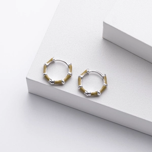 Detail of silver bamboo style earrings with green enamel on a clean geometric background