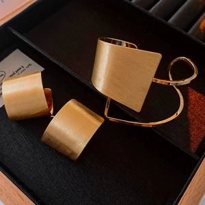 Close-up of golden matte brushed texture on geometric bracelet and earring jewelry set