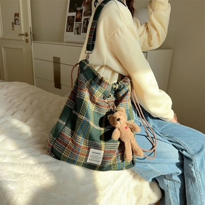 Detailed side view of green plaid wool tote bag with brown plush bear charm in warm lighting