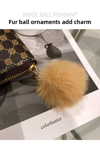 Detail of the soft faux fur pompom charm and metal zipper on the brown patterned wallet