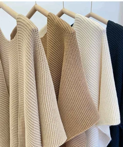 Detailed view of thick knitted shawls in beige, khaki, and cream on wooden hangers
