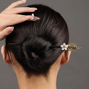 Close-up of a wooden hair stick with shell flower and golden leaf detail on a model