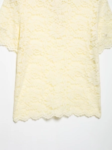 Close-up of intricate lace patterns and scalloped hem on this pale yellow polo top