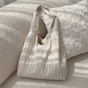 Close-up of pleated cream tote bag with smooth texture under soft natural light shadows