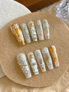 Detail of handmade Christmas press-on nails with 3D white snowflakes and golden mirror finish