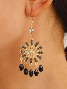 Close-up of bohemian gold sunburst earrings with black teardrop beads on a model