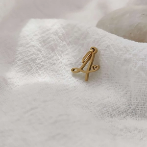 Macro view of 14K gold plated stainless steel letter pendant on soft white fabric texture