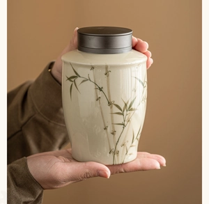 Detail of hand-painted bamboo ceramic tea canister with an alloy lid held by hands