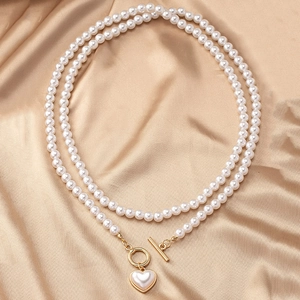 Double-layered pearl necklace with golden heart pendant on luxury champagne silk background