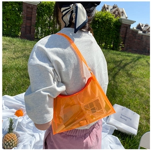 Detailed view of orange transparent PVC shoulder bag worn outdoors in a sunny park