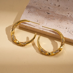 Dettaglio macro di orecchini a cerchio ritorti a C in oro 18k con zirconi cubici micro-pavé
