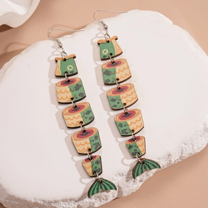 Detail of fish-shaped wooden earrings with retro green and orange patterns on a stone base