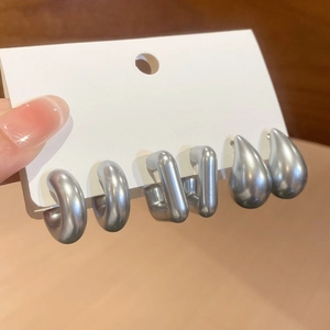 Close-up of three pairs of silver-gray acrylic hoop and teardrop earrings on a card