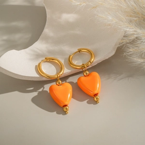 Créoles dorées avec pendentifs cœur orange présentées sur un fond minimaliste chic