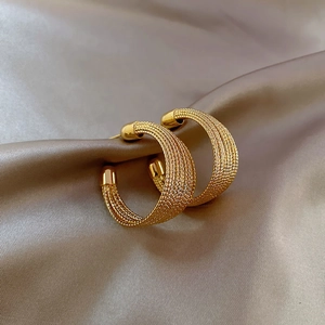 Detailed close-up of gold woven texture hoop earrings on champagne silk fabric