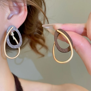 Détail de créoles gouttes en métal avec pendentif ovale en bois au style rétro