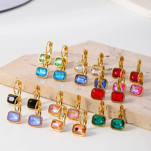 Golden hoop earrings with colorful rectangular zircon crystals displayed on a stone plate