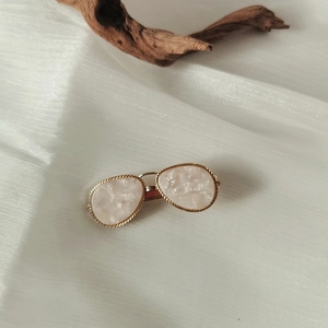 Close-up of golden metal hair clip with white resin inlay on textured white fabric