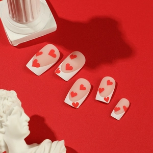 French tip press-on nails with red heart patterns on a vibrant red background