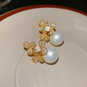 Detailed close-up of golden floral stud earrings with tiny crystals and large white pearls