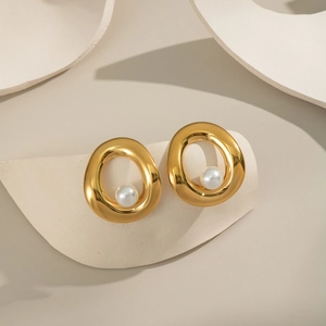 Close-up of elegant gold oval pearl earrings displayed on a curved minimalist prop
