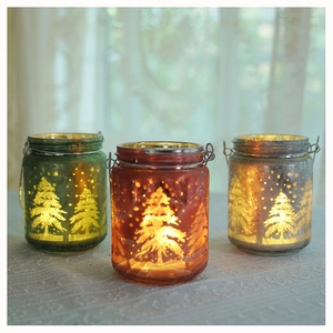 Close-up of three festive frosted glass candle jars with elk and Christmas tree patterns