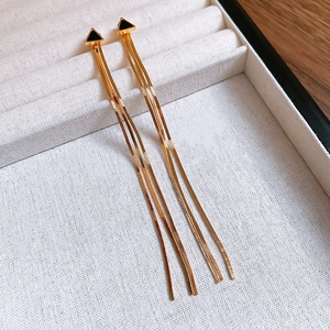 Détail de boucles d'oreilles à pompons dorés avec clous triangulaires noirs sur plateau
