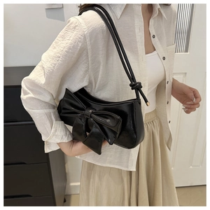 Close-up of glossy black bow shoulder bag featuring a polished faux leather finish