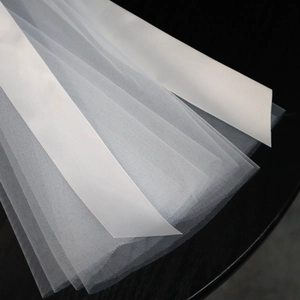 Detailed close-up of white multi-layer bridal veil with satin edges on black background
