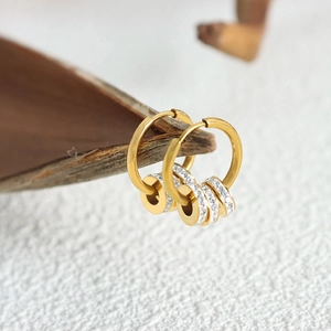 Elegante goldene Creolen mit drei kristallbesetzten Zylinder-Anhängern auf grauem Grund