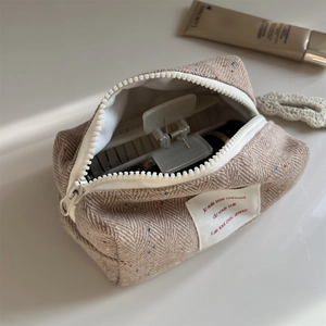 Macro detail of herringbone wool cosmetic bag with colorful flecks and zip closure