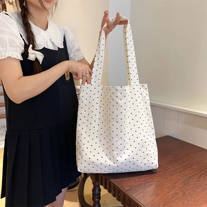 Detailed side view of white polka dot canvas tote bag shown in a cozy indoor setting