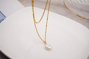 Macro shot of double-layer gold chain necklace with a baroque pearl pendant and leaf detail