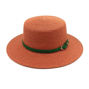 Détail d'un chapeau de paille orange avec bande en cuir vert et boucle dorée