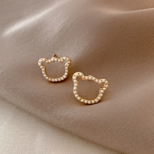 Macro shot of gold bear-shaped earrings with white pearls on elegant silk fabric