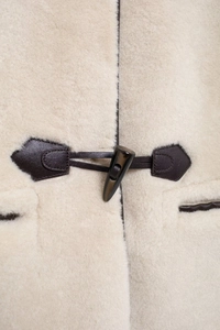 Dettaglio dell'alamaro e della pelle marrone sul cappotto di pelliccia crema