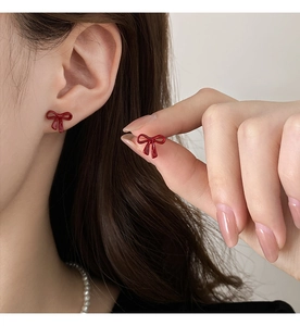 Close-up of elegant red bow earrings with glossy enamel finish on model ear